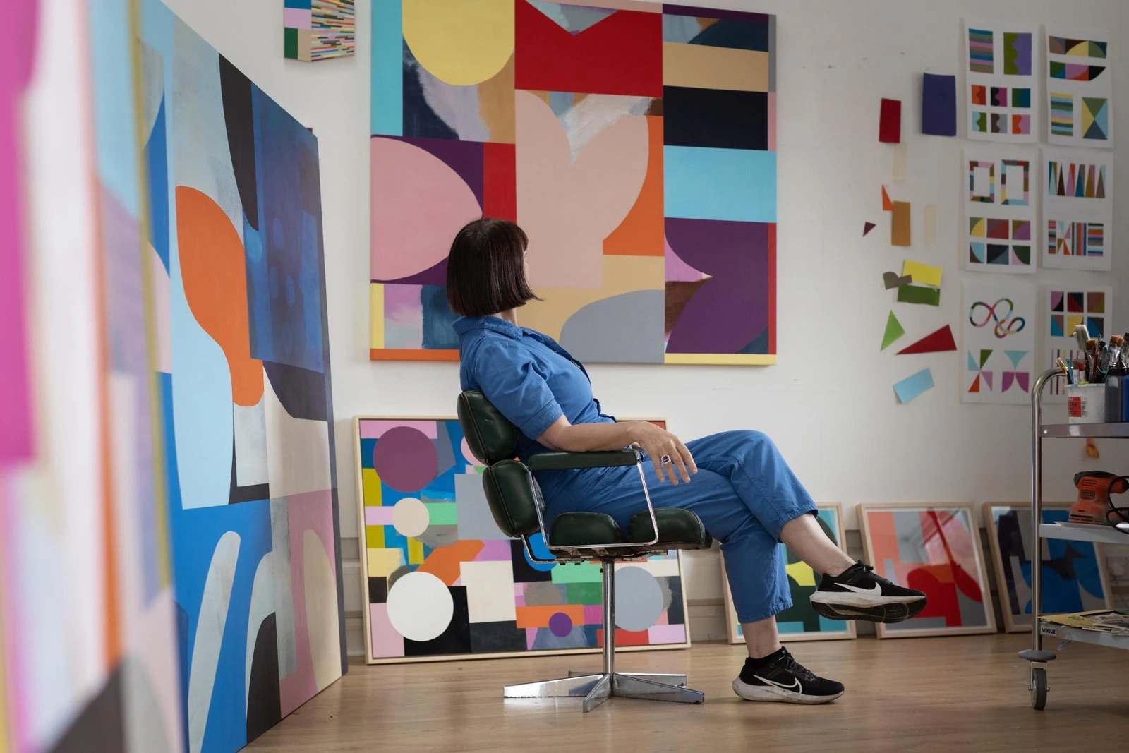 Portrait of Mary O'Connor seated in her studio in front of her bold, colourful abstract geometric paintings