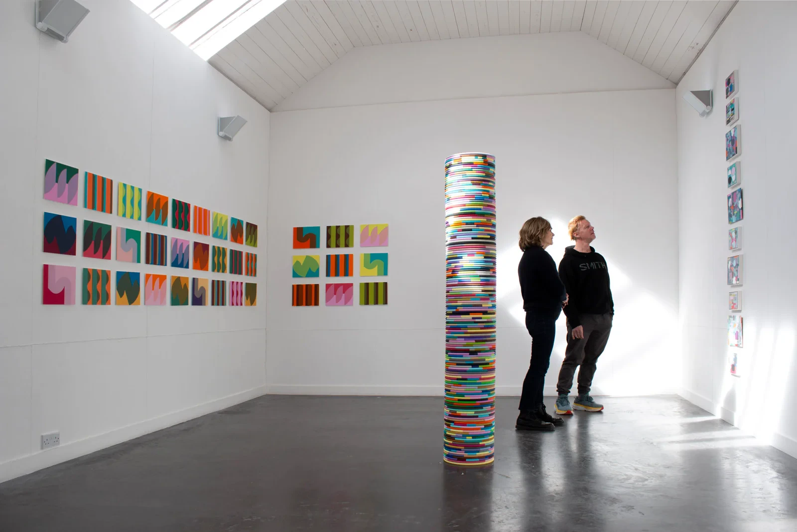 Two visitors viewing Mary O'Connor's tall stacked-panel column at the 'Linked' exhibition, Ballinglen Arts Foundation, 2025